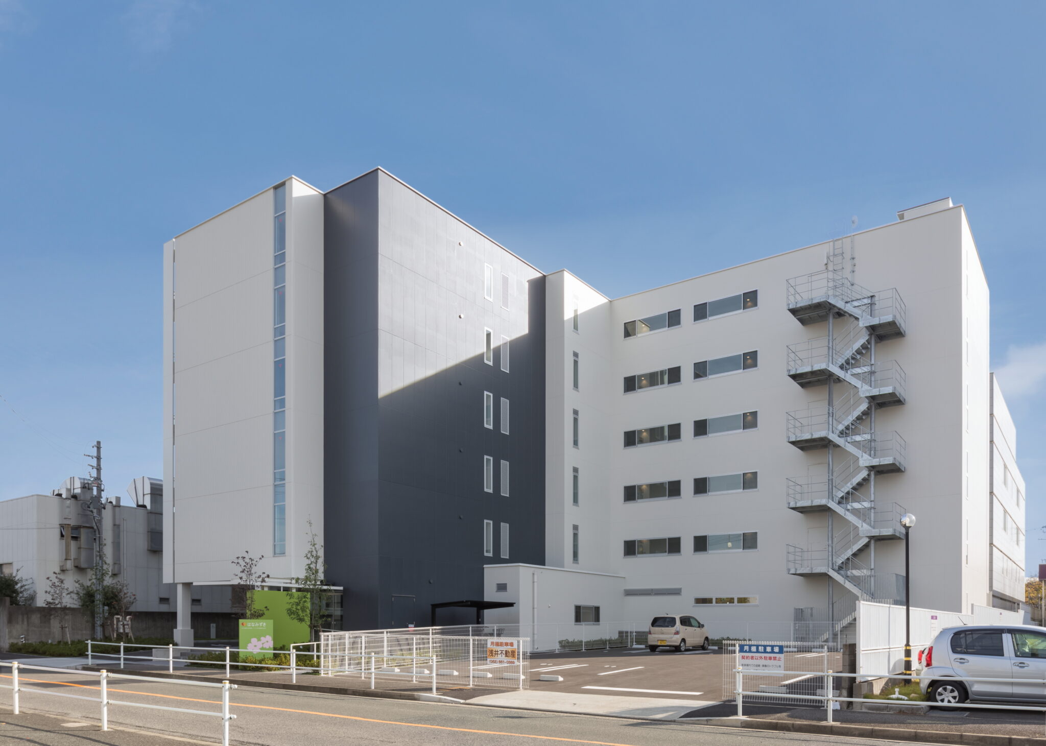 複数棟の介護施設建物。モダンな白黒配色の多層階建築と駐車場が見える。
