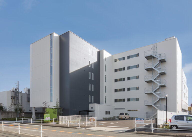 モダンデザインの介護施設建物。白と黒の外壁、複数階建て、駐車場完備。